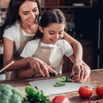 Woman and young girl in aprons preparing vegetables together in a kitchen.