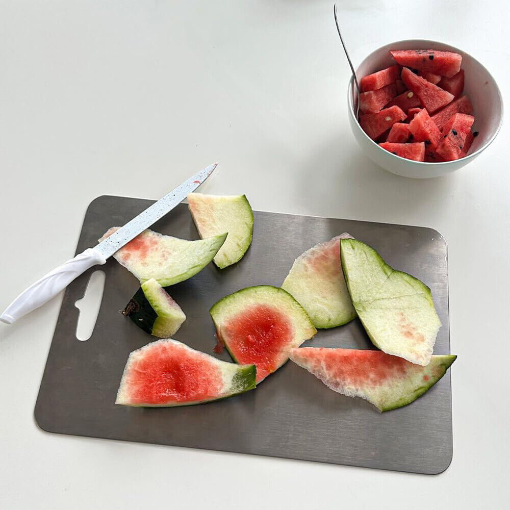 Gray cutting board on a kitchen counter with various kitchen items.

