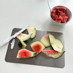 Gray cutting board on a kitchen counter with various kitchen items.

