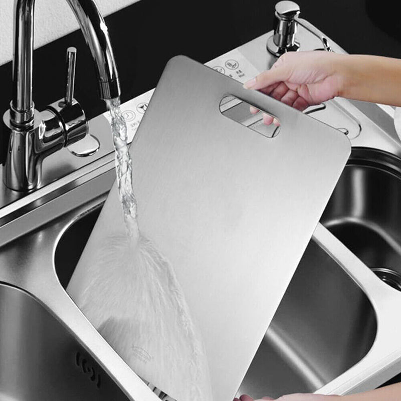 Person washing a cutting board under running water in a kitchen sink