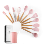 Set of pink and wooden kitchen utensils with a pink container and black box on a white background.