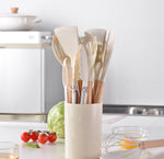 Set of kitchen utensils in a holder on a kitchen counter with vegetables and a whisk.